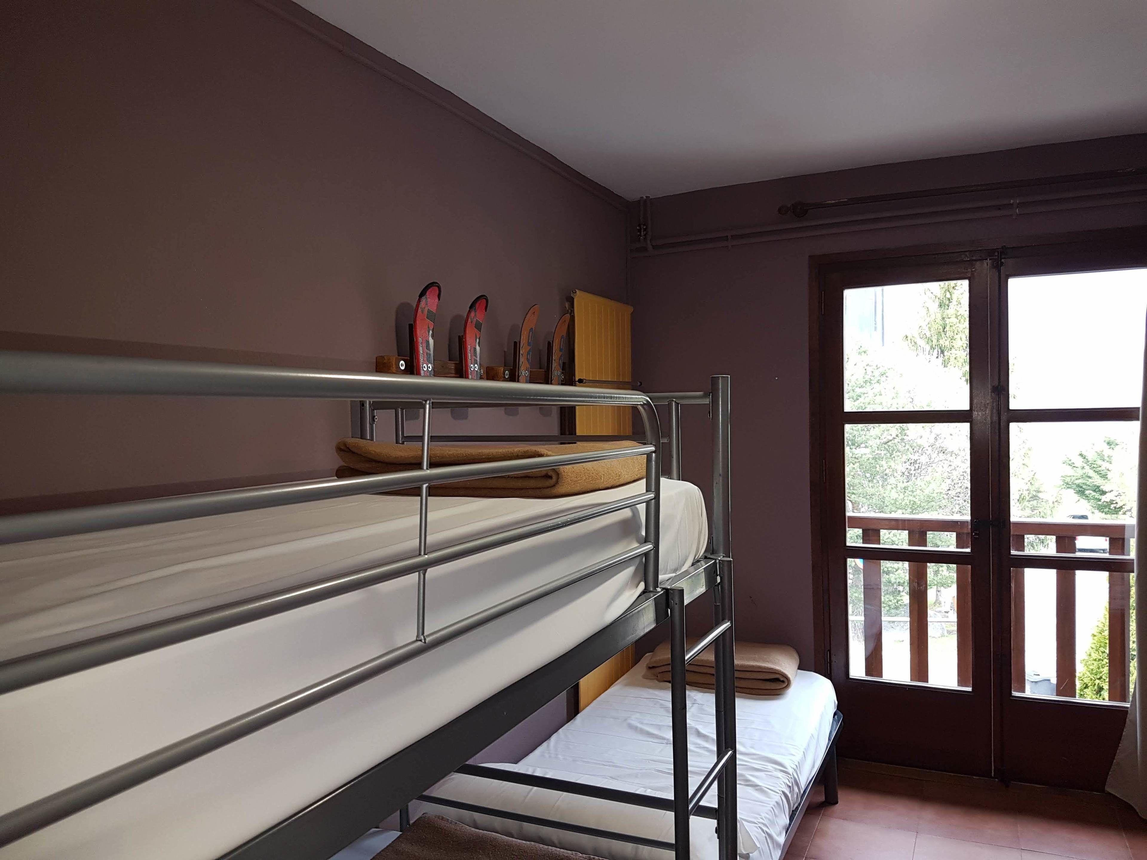 Een studentenkamer met stapelbedden, een raam met uitzicht op groen en een deur.