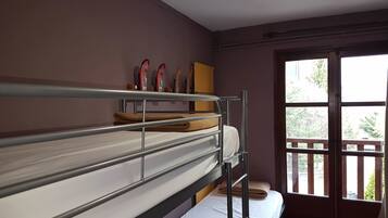 Een studentenkamer met stapelbedden, een raam met uitzicht op groen en een deur.