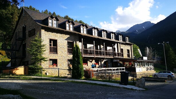 A stone building with multiple balconies and a ski lift, surrounded by mountains. - Alberg Les Daines (Espot)