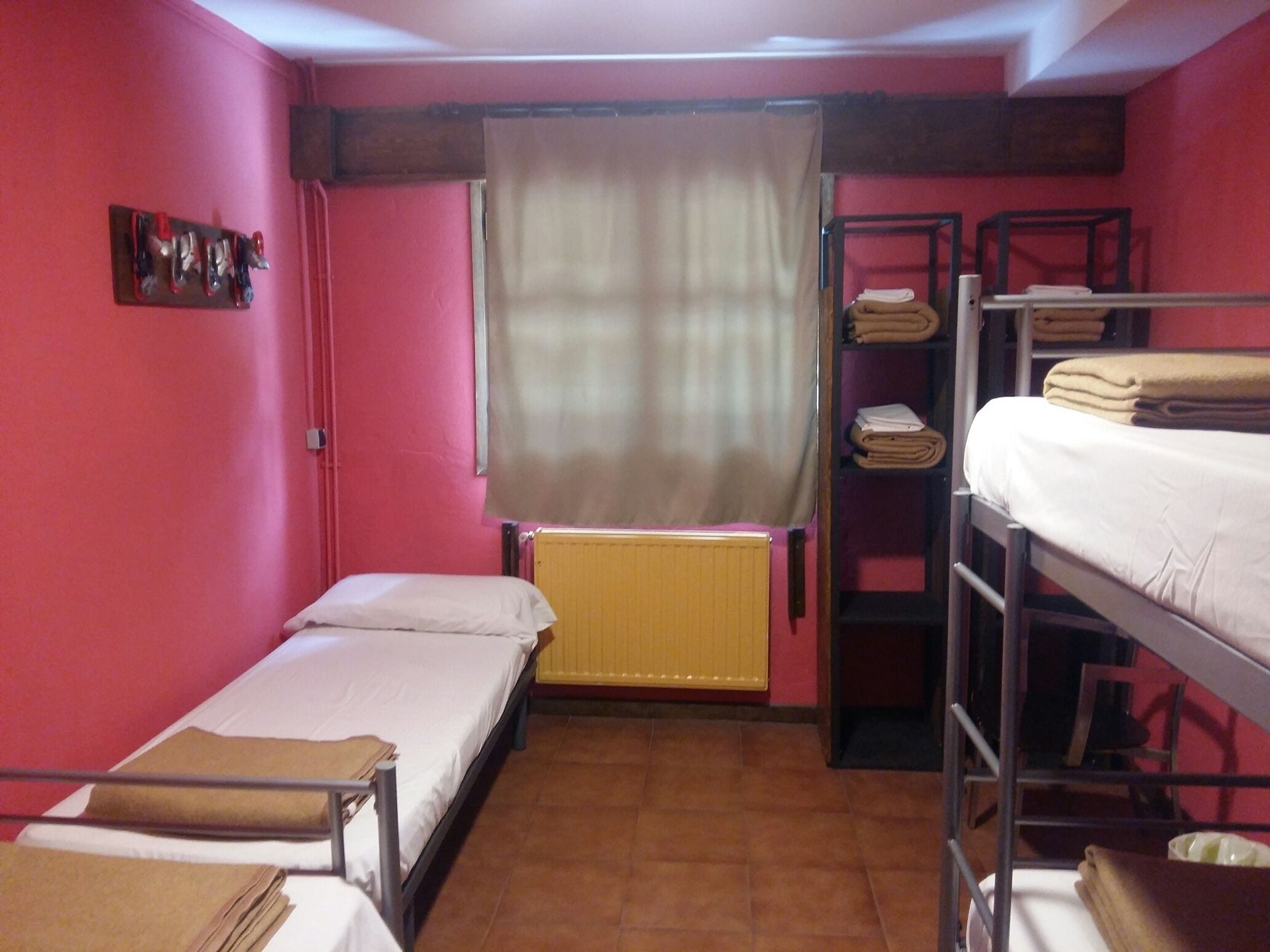 Une chambre de dortoir avec deux lits simples, un radiateur, une fenêtre avec un rideau et un lit superposé avec des couvertures pliées.