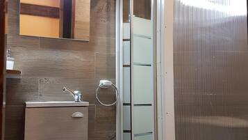 A bathroom with a wooden wall, a mirror, a sink with a faucet, a toilet, and a shower enclosure.
