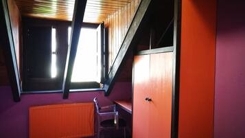 Una habitación con techo inclinado, una ventana, un radiador y una silla.