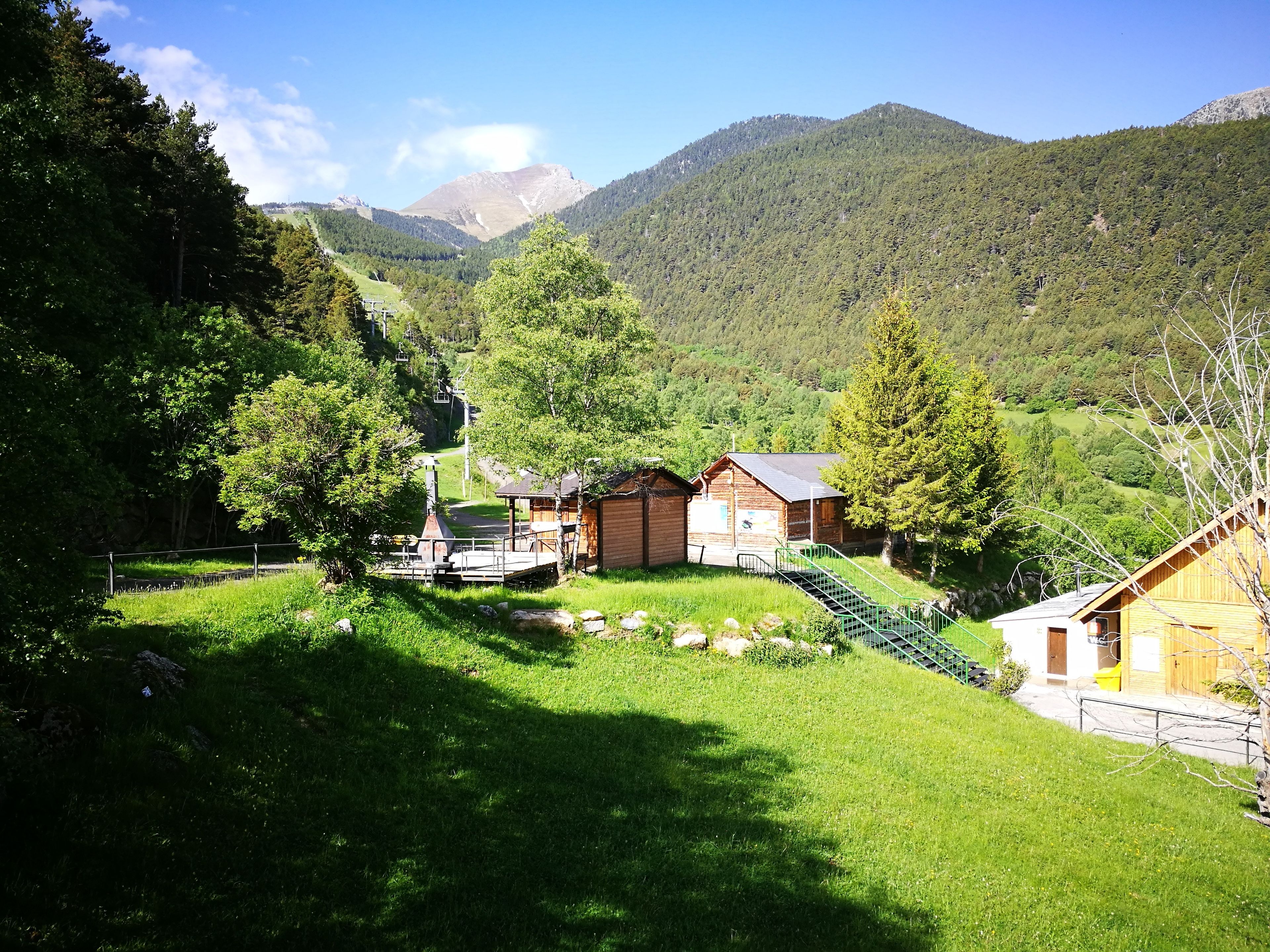 A rustic cabin with a wooden exterior, surrounded by lush greenery and mountains in the background.