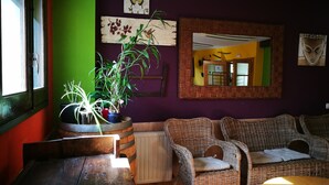 A room with a green wall, a wooden table, wicker furniture, and a mirror. - Alberg Les Daines (Espot)