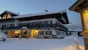 A large, multi-story building with a snow-covered exterior, balconies with railings, and a lit entrance.