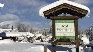 A sign for Egglerlehen, a guesthouse and holiday homes, with a snowy landscape and mountains in the background.