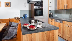 A compact kitchen with wooden cabinets, a built-in oven, and a dining area with a bench and table.