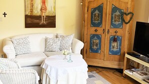 Un soggiorno con un divano, un tavolino con un vaso, un mobile in legno con icone religiose e una televisione.