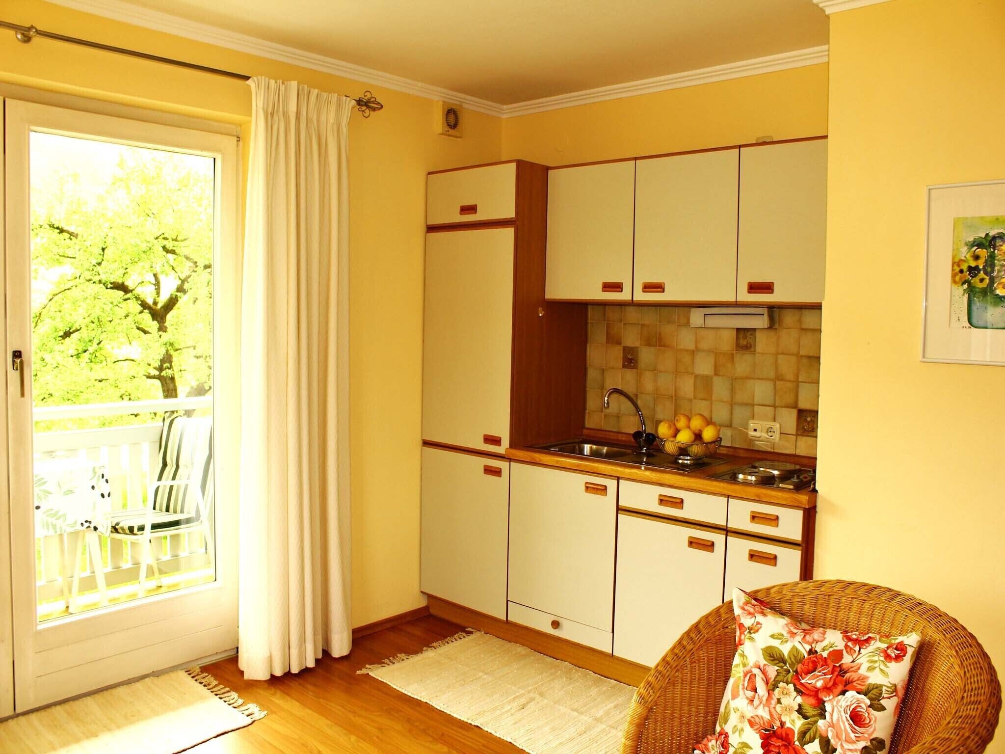 Cocina compacta con armarios blancos, un lavamanos y un ventanal con cortinas.