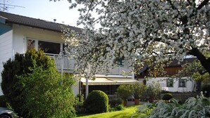 Un edificio residenziale con un balcone, una strada di accesso lastricata e un giardino curato con piante fiorite.