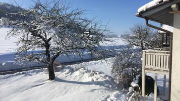 A snow-covered landscape with a house and a tree in the foreground.