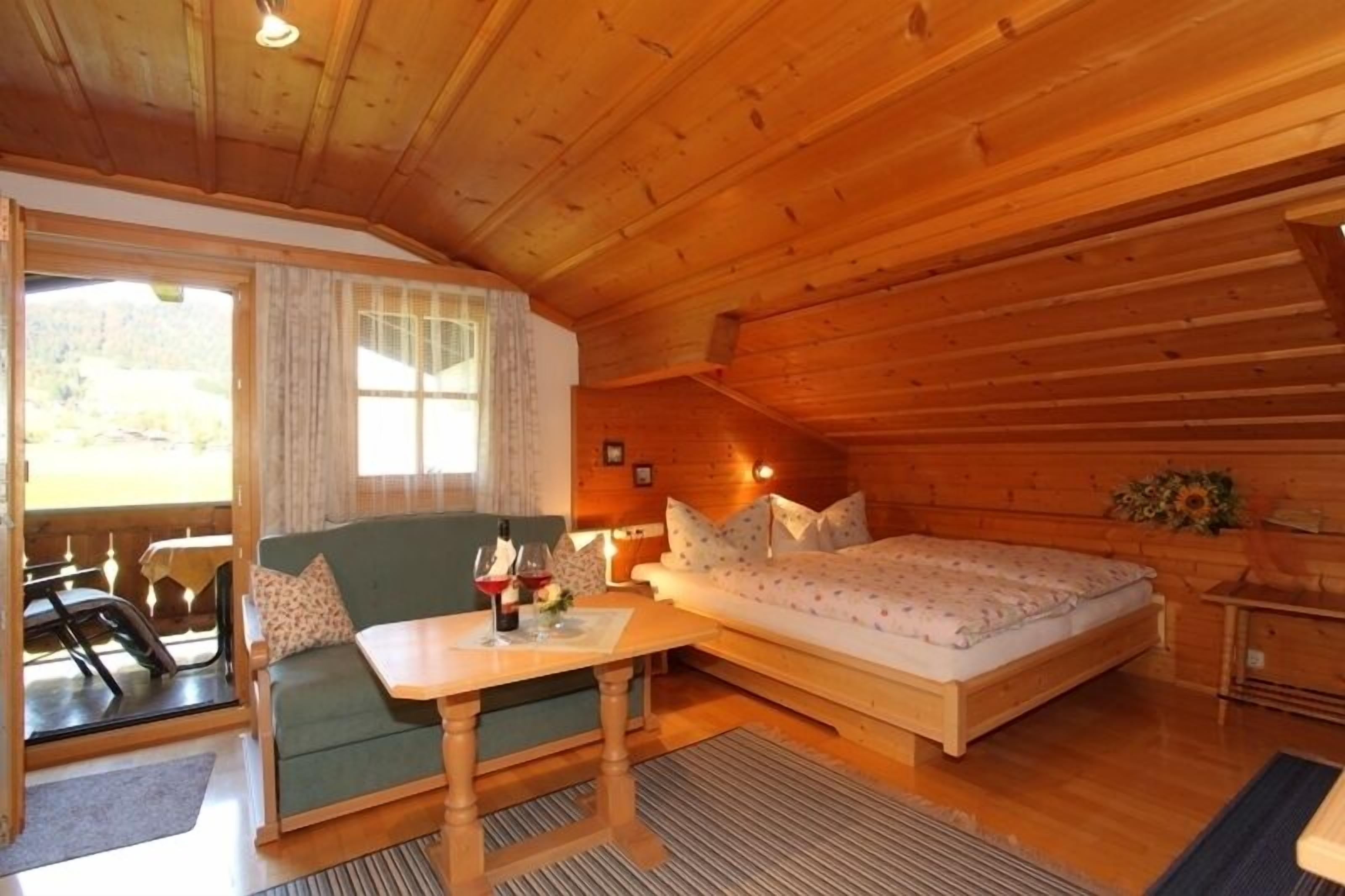 Een knus vakantiehuisje met houten inrichting, een bank, een bed en een eettafel met wijnglazen.