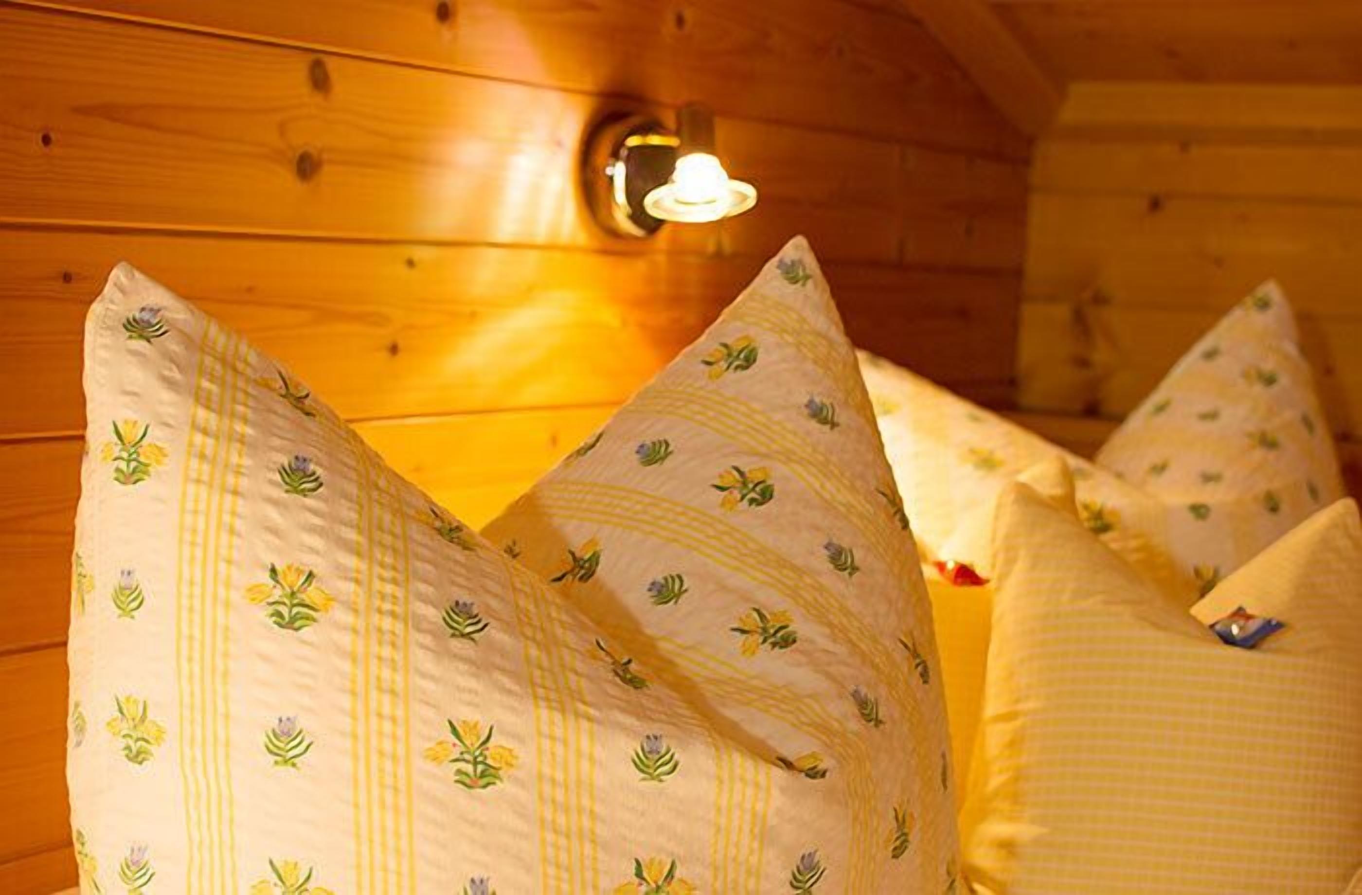 A wooden cabin interior with a bed featuring pillows with floral patterns.