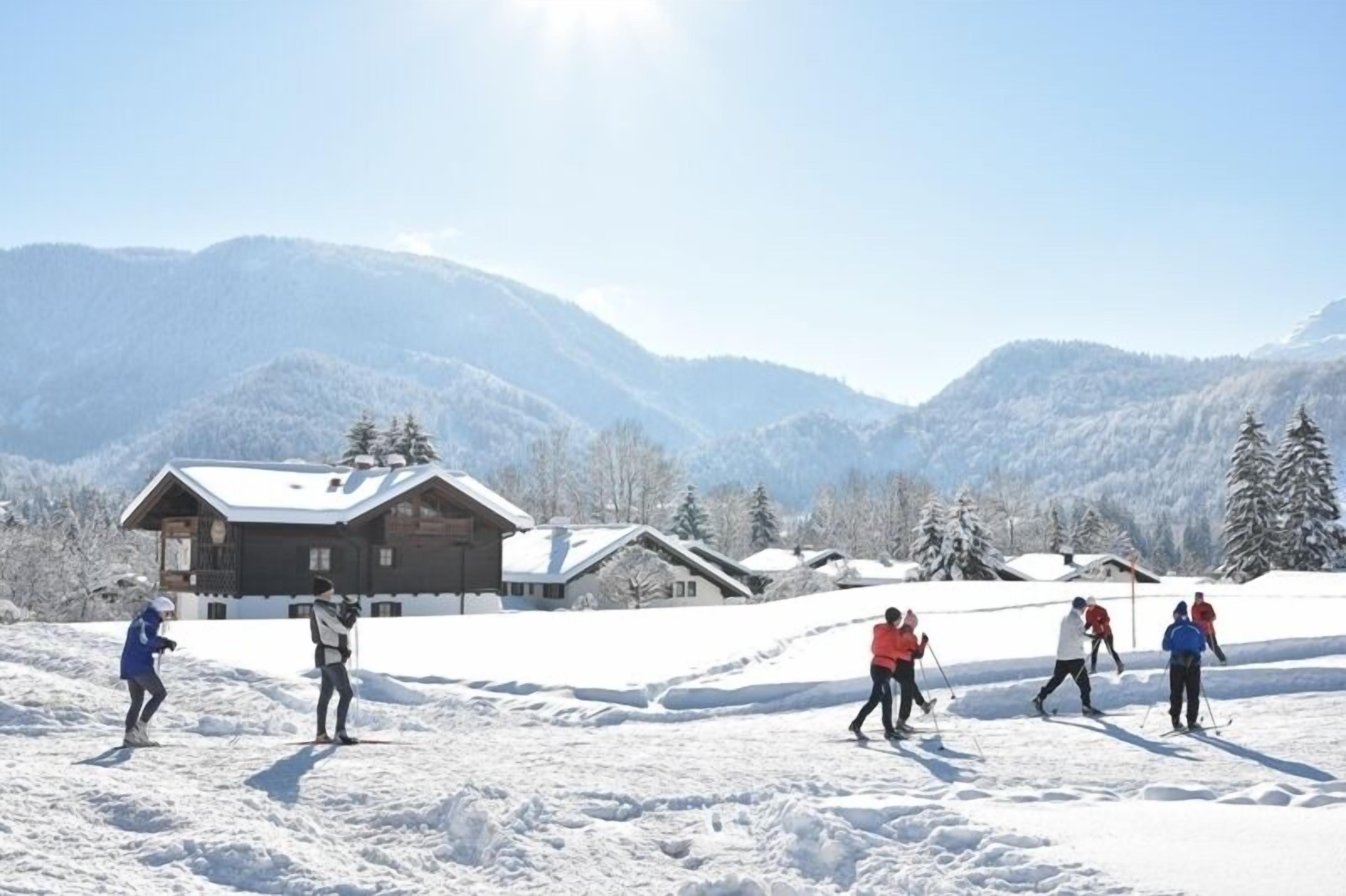 A snow-covered landscape with a wooden cabin and a group of people skiing.