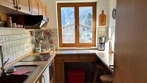 A kitchen with wooden cabinets, a tiled backsplash, a window with a view, and a red storage box. - Ferienwohnung 60 m², 1-2 Personen, Schlafzimmer, Kabel-TV, Balkon, Nichtraucher (Unterwössen)
