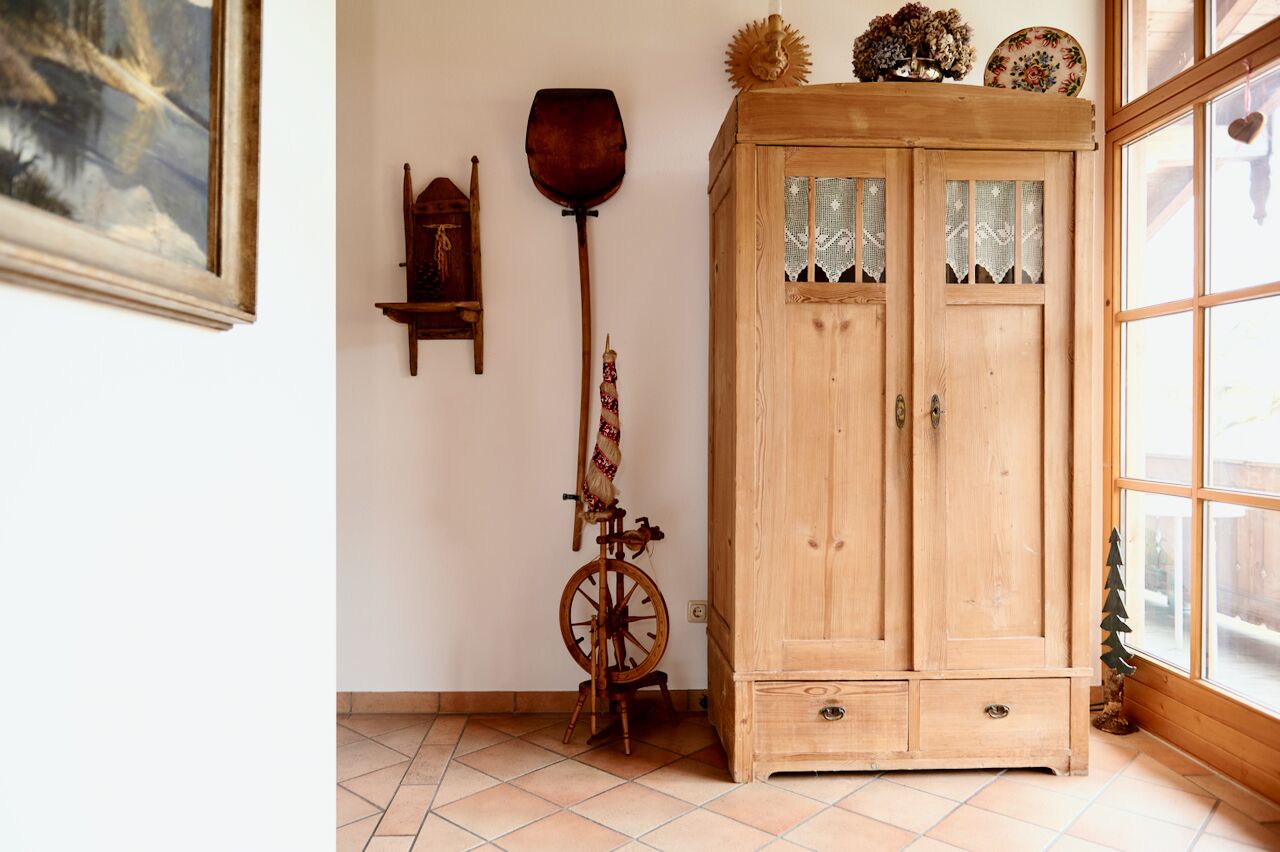 A wooden cabinet with glass doors, a spinning wheel, and a small wooden shelf with decorative items.