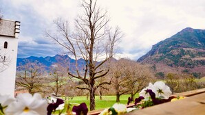 A view of a mountainous landscape with a white building and a large tree in the foreground. - Vacation apartment 60sqm (Brannenburg)