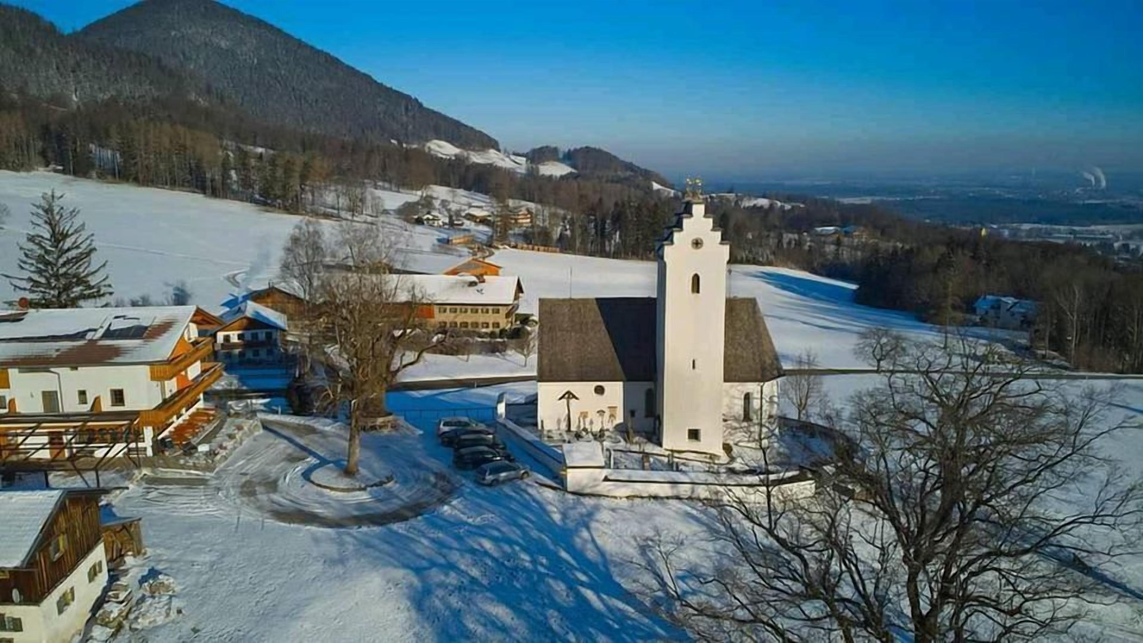 Eine Kirche mit einem Glockenturm, umgeben von schneebedeckten Feldern und Bergen.