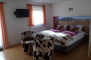 Quarto com cama, televisão na parede e janela com cortinas.