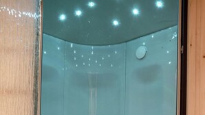 Ein kleiner, abgeschlossener Duschbereich mit gebogenem Boden und einem einzelnen Wasserhahn.