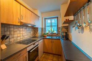 A modern kitchen with wooden cabinets, a built-in stove, and a window with curtains.