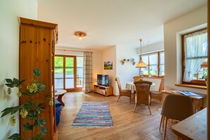 A spacious living area with a television, dining table, chairs, and a colorful rug.