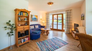 A cozy living room with a wooden bookshelf, a blue sofa, a round coffee table, and a wicker chair. - Apartment Unternberg 58sqm balcony, kitchen, 1 bedroom, 1 bed-sitting room, 2 p. (Ruhpolding)
