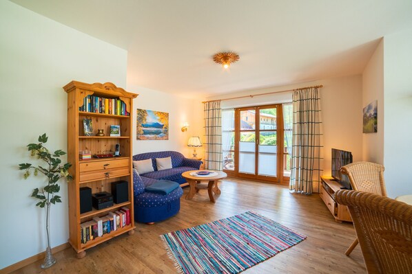 Een gezellige woonkamer met een houten boekenkast, een blauwe bank, een ronde salontafel en een rieten fauteuil.
