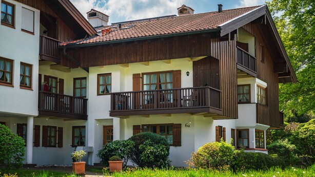 A two-story building with balconies, a garden, and a sign indicating the number of rooms. - Apartment Unternberg 58sqm balcony, kitchen, 1 bedroom, 1 bed-sitting room, 2 p. (Ruhpolding)