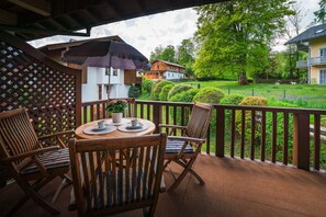 Une terrasse en bois avec une table et des chaises, un pot de fleurs et une vue sur un paysage verdoyant parsemé de maisons.