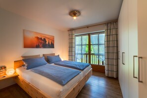 A bedroom with two beds, a large window with curtains, a painting on the wall, and a ceiling light.