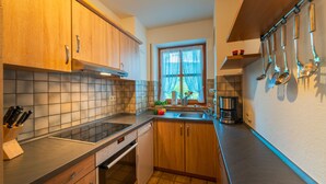 A modern kitchen with wooden cabinets, a tiled backsplash, a built-in oven, and a window with curtains. - Apartment Unternberg 58sqm balcony, kitchen, 1 bedroom, 1 bed-sitting room, 2 p. (Ruhpolding)