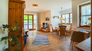 A spacious living room with a wooden floor, a television, a dining area with chairs, and large windows with curtains. - Apartment Unternberg 58sqm balcony, kitchen, 1 bedroom, 1 bed-sitting room, 2 p. (Ruhpolding)