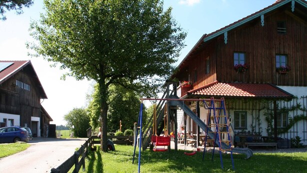 Un'area giochi con scivolo e altalene, una recinzione in legno e un edificio con tetto rosso.