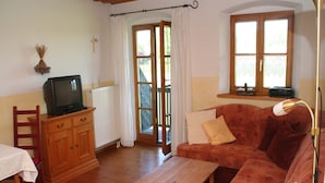 Un accogliente soggiorno con un tavolo di legno, un divano rosso, una televisione su un mobile e una finestra con tende.