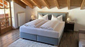 Een slaapkamer met een houten plafond, een groot bed met witte beddengoed, twee nachtkastjes met lampen en een uitzicht op een buitenruimte door een raam.