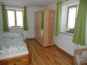Un dormitorio con una cama y un armario de madera, una ventana con cortinas verdes y un radiador.