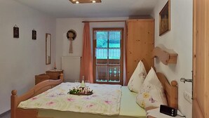 A bedroom with a bed, a dresser, a mirror, a window with curtains, and a door. - Ferienwohnung für 1-2 Personen, ca. 45qm (Marktschellenberg)