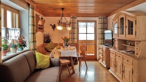 A cozy living room with a sofa, a dining table with chairs, and wooden cabinets. - Ferienwohnung für 1-2 Personen, ca. 45qm (Marktschellenberg)