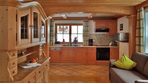 A cozy kitchen with wooden cabinets, a built-in oven, and a dining area with a sofa. - Ferienwohnung für 1-2 Personen, ca. 45qm (Marktschellenberg)