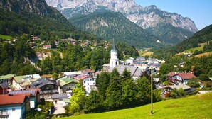 A mountain village with a prominent church, surrounded by lush greenery and rocky mountains. - Ferienwohnung für 1-2 Personen, ca. 45qm (Marktschellenberg)