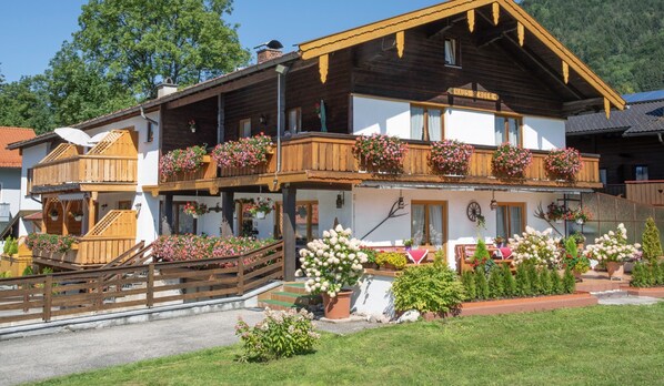 Un chalet traditionnel en bois, doté de balcons ornés de fleurs, d’un escalier en bois et d’un jardin bien entretenu.