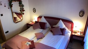 Un lit double avec une couvre-lit à carreaux, un miroir orné d’un cadre floral et un plafond en bois.
