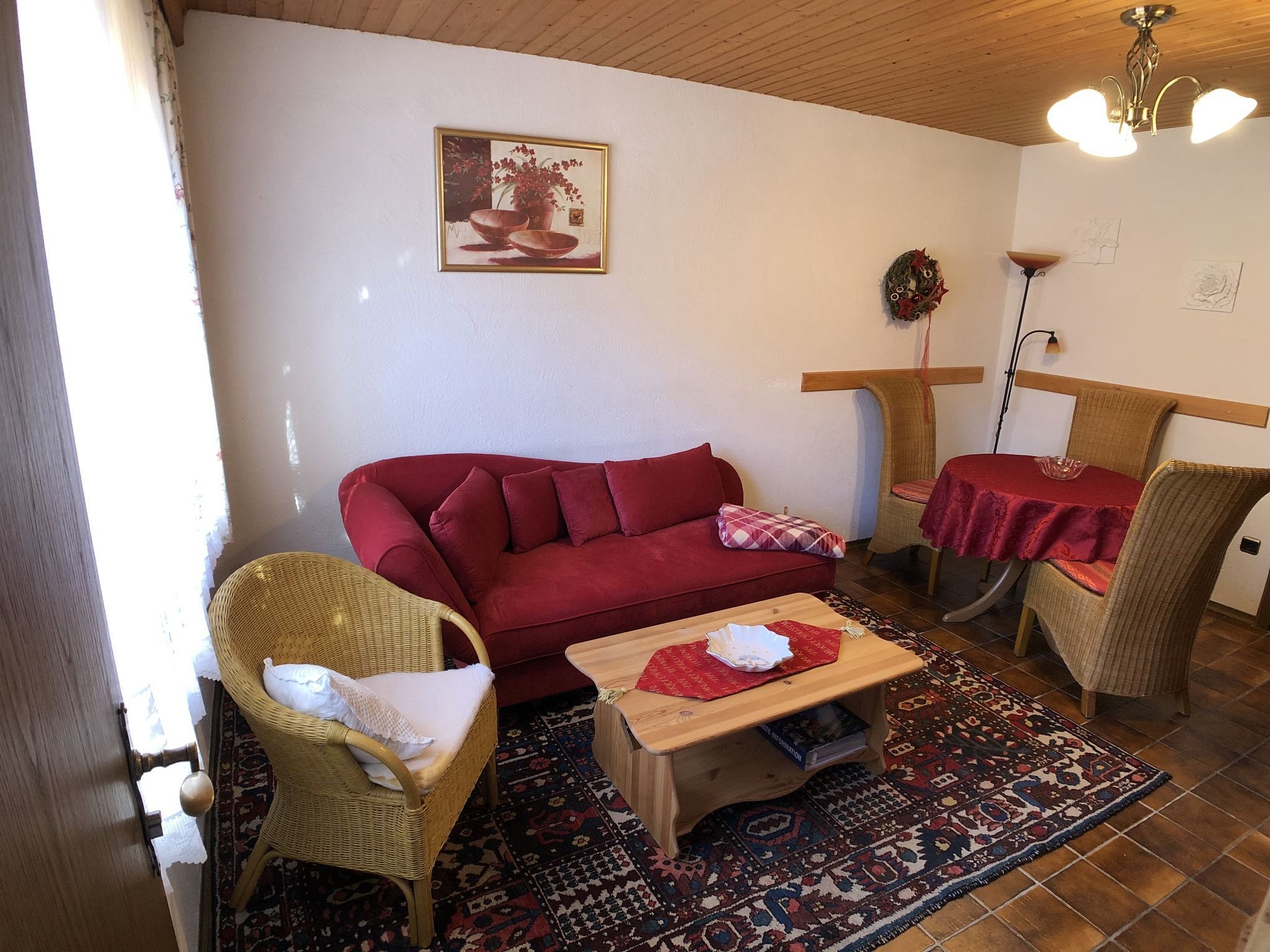 Un soggiorno accogliente con un divano rosso, poltrone in vimini, un piccolo tavolino in legno, un tappeto decorato e un quadro appeso al muro.