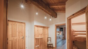 Un pasillo con puertas de madera, una silla, una cama y una cocina al fondo.