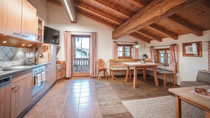 Una cocina rústica con armarios de madera, un comedor con mesa y bancos de madera, y un ventanal con cortinas.