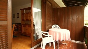 Un balcone in legno con una sedia di plastica bianca e un tavolino, una porta scorrevole in vetro e mobili in legno sullo sfondo.