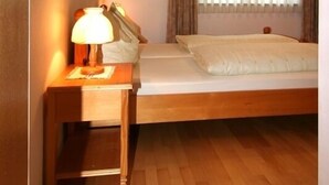 Una camera compatta con un letto singolo, un comodino con una lampada, una finestra con tende e un lampadario.