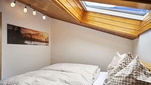 Un dormitorio con tragaluz, una cama con ropa de cama a cuadros y un cuadro de un paisaje montañoso.