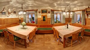 A dining area with wooden tables and chairs, a central bench, and a view of the outdoors through windows. - Cozy vacation apartment 3, 25 sqm (Schneizlreuth)